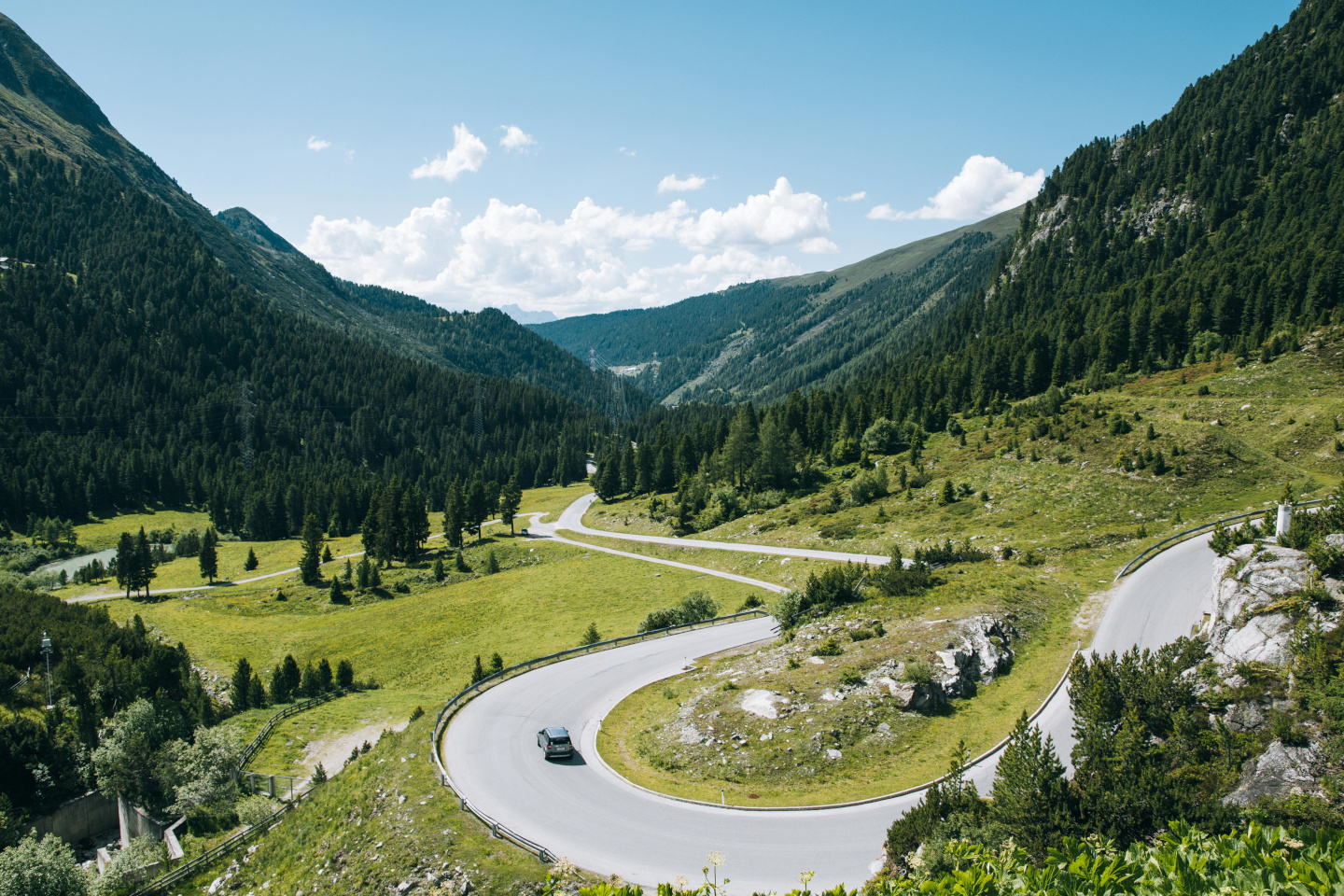 Mountain valley with green grass, trees, and a winding road