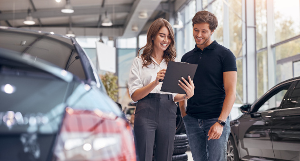 Employee Showing Clipboard to Customer Smiling car dealer employee presenting warranty paperwork to pleased customer at certified dealership